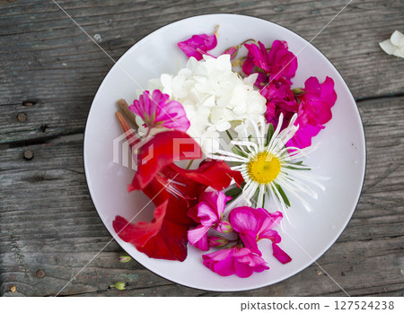 On a white plate beautiful multi-colored flowers on a wooden background 127524238