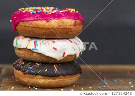 Lovely sweet food. Stack of glazed colorful assorted donuts with splashes on a gray background. Lovely sweet food. Stack of glazed colorful assorted donuts with splashes on a gray background. 127524248