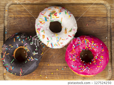 Beautiful sweet food. Stack of glazed colorful assorted donuts on a wooden background. Beautiful sweet food. Stack of glazed colorful assorted donuts on a wooden background. 127524250