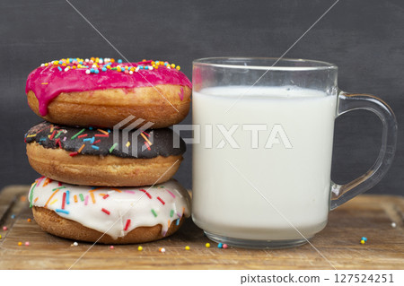 Lovely sweet food. Stack of glazed colorful assorted donuts with a cup of milk on a gray background. 127524251
