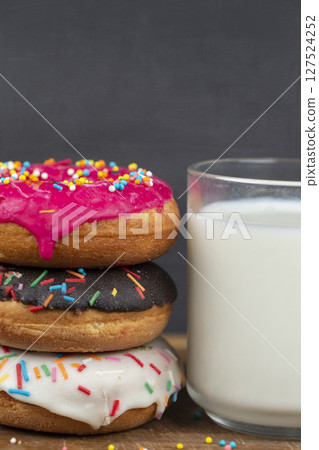 Lovely sweet food. Stack of glazed colorful assorted donuts with a cup of milk on a gray background. Lovely sweet food. Stack of glazed colorful assorted donuts with a cup of milk on a gray background. 127524252