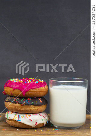 Lovely sweet food. Stack of glazed colorful assorted donuts with a cup of milk on a gray background. 127524253