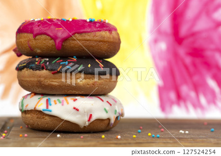Creative sweet food. A stack of glazed colorful assorted donuts on a bright watercolor painted background. 127524254