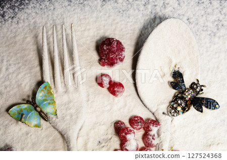 A spoon and a fork, red berries are sprinkled with flour and a brochure in the form of insects lies at the top. Creative food preparation. 127524368