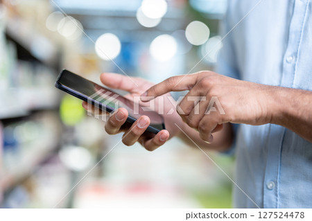 A person's hands are using a smartphone, possibly in a store. The image is well-lit and the focus is on the phone. 127524478