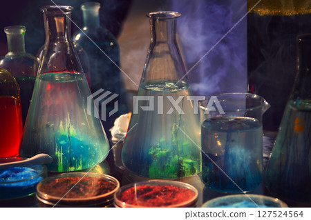 Biology laboratories. Green plants in glass bottles on a dark background. In flasks, medium for bacteria. Mystical laboratory. 127524564