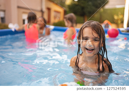 Young girl swimming joyfully in backyard pool during sunny day 127524595