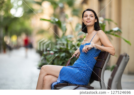 Young woman sits on bench on city street Young woman sits on bench on city street 127524696