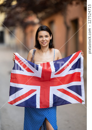 Young girl holding national flag of UK flag, standing outdoors Young girl holding national flag of UK flag, standing outdoors 127524715