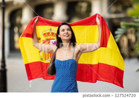 Patriotic young brunette girl waving the flag of Spain on city street Patriotic young brunette girl waving the flag of Spain on city street 127524720