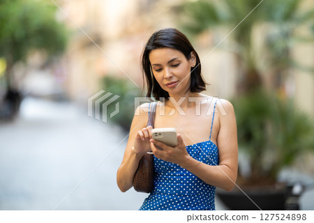 Happy young girl with mobile phone in her hands walking around city and taking pictures of sights 127524898