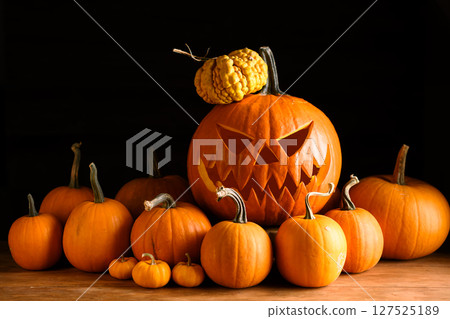Scary jack-o'-lantern in center of tiny orange pumpkins 127525189