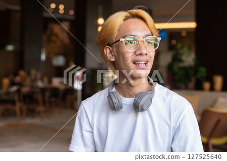 Face of Asian teenager man with blonde hair inside cafe restaurant smiling 127525640