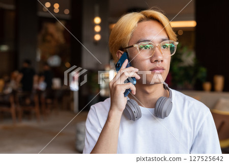 Asian teenager man with blonde hair inside cafe restaurant talking on phone Asian teenager man with blonde hair inside cafe restaurant talking on phone 127525642