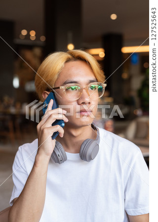 Asian teenager man with blonde hair inside cafe restaurant talking on phone Asian teenager man with blonde hair inside cafe restaurant talking on phone 127525643