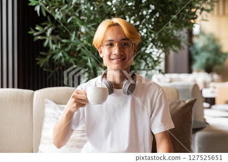Asian teenager man with blonde hair inside cafe restaurant holding coffee cup Asian teenager man with blonde hair inside cafe restaurant holding coffee cup 127525651