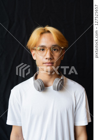 Studio portrait of young gay man with septum piercing ring and headphones 127525657