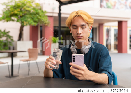 Asian gay teenager drinking water and using phone outdoors in cafe restaurant Asian gay teenager drinking water and using phone outdoors in cafe restaurant 127525664