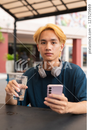 Asian gay teenager drinking water and using phone outdoors in cafe restaurant Asian gay teenager drinking water and using phone outdoors in cafe restaurant 127525669