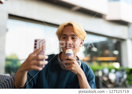 Young man eating soft serve ice cream outdoors while taking selfie with phone Young man eating soft serve ice cream outdoors while taking selfie with phone 127525719