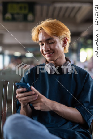 Young Asian tourist man in bus station texting with phone 127525722