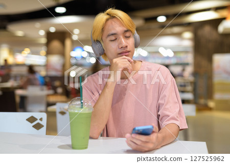 Thai gay teen man with headphones listening music in cafe 127525962