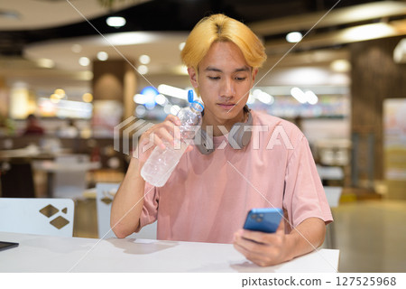 Young student teenager man with headphones drinking water and using mobile phone 127525968