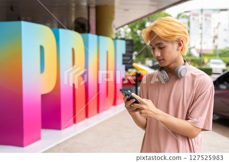 Young gay man using phone during pride festival 127525983