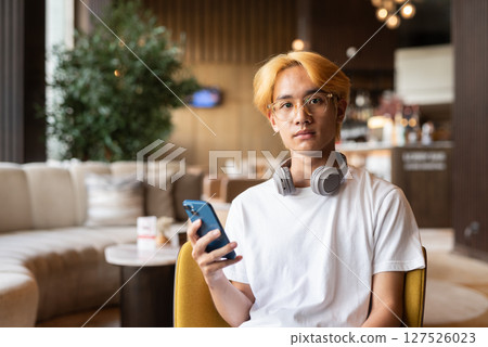 Asian teenager man with blonde hair inside cafe restaurant using phone 127526023