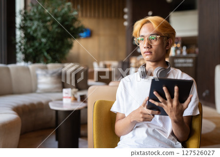 Asian teenager man with blonde hair inside cafe restaurant using tablet computer 127526027