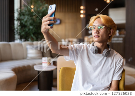 Asian teenager man with blonde hair inside cafe restaurant using phone 127526028