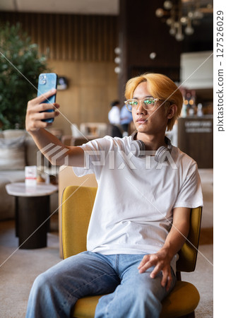 Asian teenager man with blonde hair inside cafe restaurant using phone 127526029
