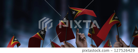 East Timor flags in their hands on a blurred urban background East Timor flags in their hands on a blurred urban background 127526429