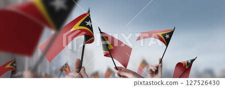 East Timor flags in their hands on a blurred urban background East Timor flags in their hands on a blurred urban background 127526430