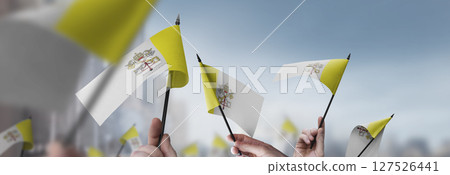 Vatican flags in their hands on a blurred urban background 127526441