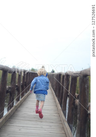 Child Running Across Wooden Bridge in Nature 127526691