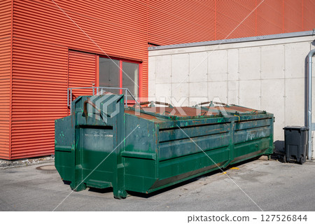 Industrial green metal dumpster near red and concrete building wall outdoors 127526844