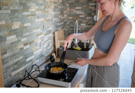 Woman cooking scrambled eggs in a frying pan on an induction cooktop, concept of home cooking 127526845