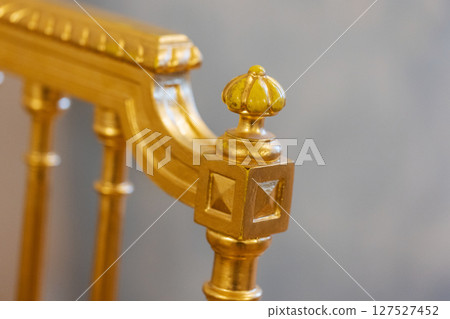 Detailed view of an ornate golden chair featuring an intricate crown finial design 127527452