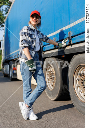 Portrait young adult smiling woman truck driver secures cargo tarp trailer truck cargo vehicle. Female person girl professional job career working driving freight engine lorry. Logistics industry Portrait young adult smiling woman truck driver secures cargo tarp trailer truck cargo vehicle. Female person girl professional job career working driving freight engine lorry. Logistics industry 127527524