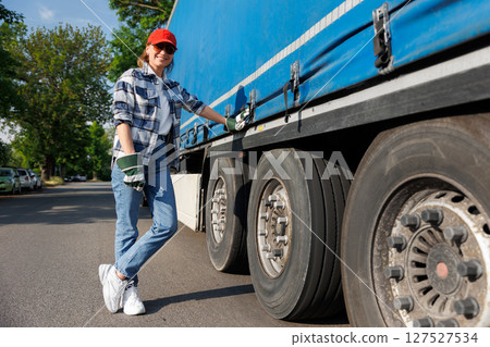 Portrait young adult smiling woman truck driver secures cargo tarp trailer truck  cargo vehicle. Female person girl professional job career working driving freight engine lorry. Logistics industry 127527534