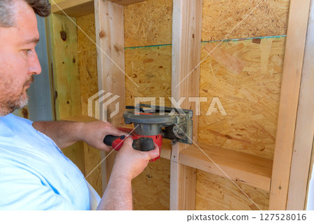 Woodworker uses saw cut router to shape wooden panels in home workshop, demonstrating skill precision. 127528016