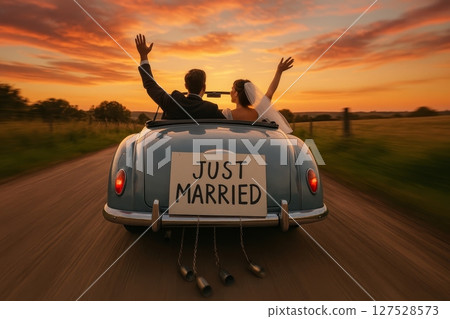 Bride and groom driving vintage car with just married sign at sunset on country road, rear view 127528573