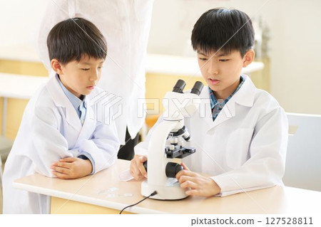 Elementary school student in a white coat using a microscope 127528811
