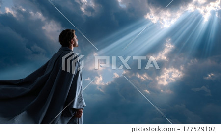 Young caucasian male gazing at sunlight beams breaking through dramatic cloudy sky. 127529102