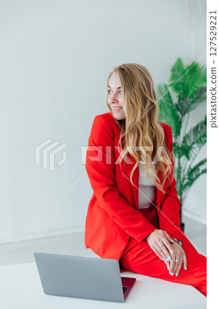 Business woman in red suit at desk with laptop working in office Business woman in red suit at desk with laptop working in office 127529221