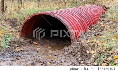 Red corrugated metal culvert pipe under road with water drainage system autumn leaves  Red corrugated metal culvert pipe under road with water drainage system autumn leaves  127529303