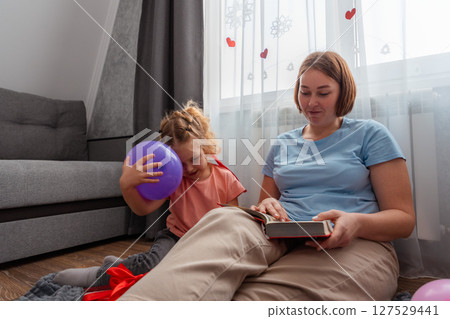 Bottom view of Caucasian young mother and little daughter are reading a book with fairy tales. Happy family spends time together. Concept of preschool education for children and Mother's Day Bottom view of Caucasian young mother and little daughter are reading a book with fairy tales. Happy family spends time together. Concept of preschool education for children and Mother's Day 127529441