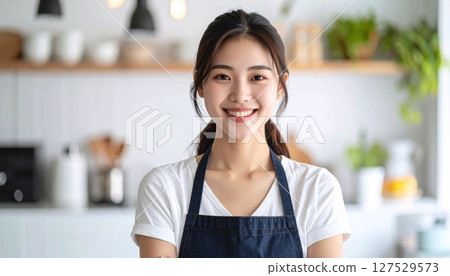 A young woman wearing an apron smiling in the kitchen 127529573