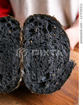 Baker Hand Presenting Homemade fresh baked black charcoal sourdough bread. Showing crumb inside. 127530311